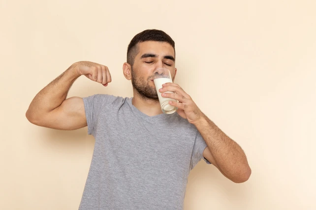 Homem tomando um copo de leite enquanto exibe o braço forte.