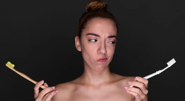 Mulher segurando duas escovas de dente, uma de bambu e uma de plástico.