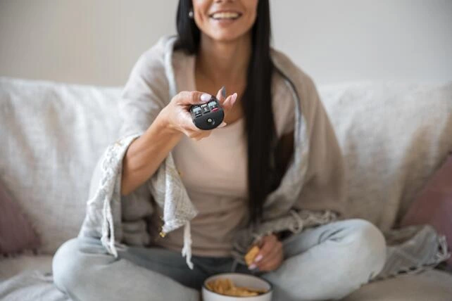 Mulher comendo, sorrindo e assistindo TV.