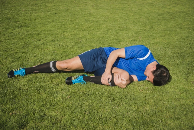 Jogador de futebol caído no chão após sofrer uma lesão por conta do dente siso.