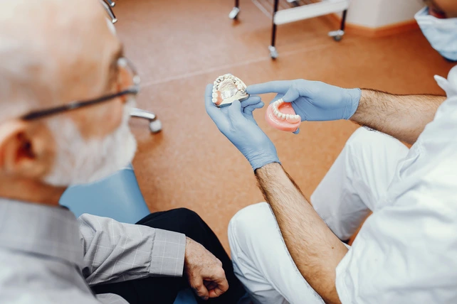 Dentista apresentando uma prótese para um paciente idoso.