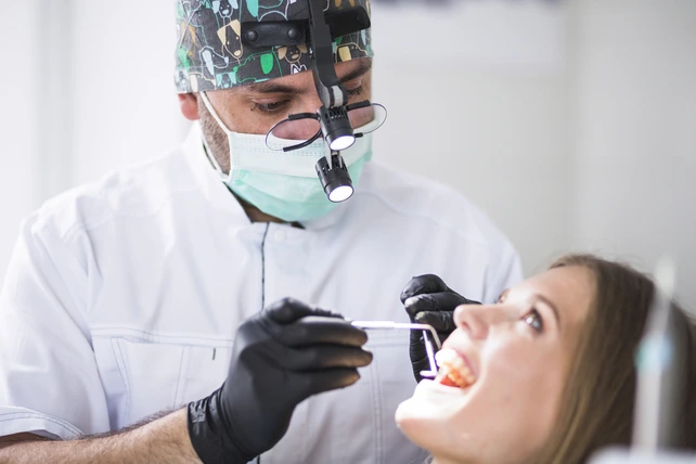Dentista homem analisando a boca de uma paciente mulher.