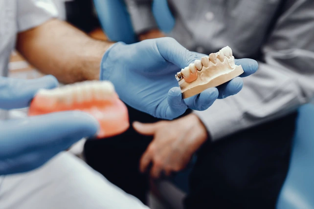 Dentista com uma ponte dentária na mão.